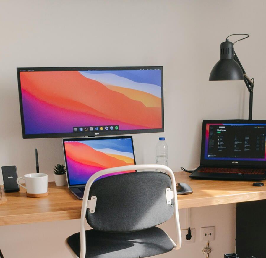Laptop, external monitor, and additional recording equipment on a wooden modern desk with a gray and white office chair in front of it.